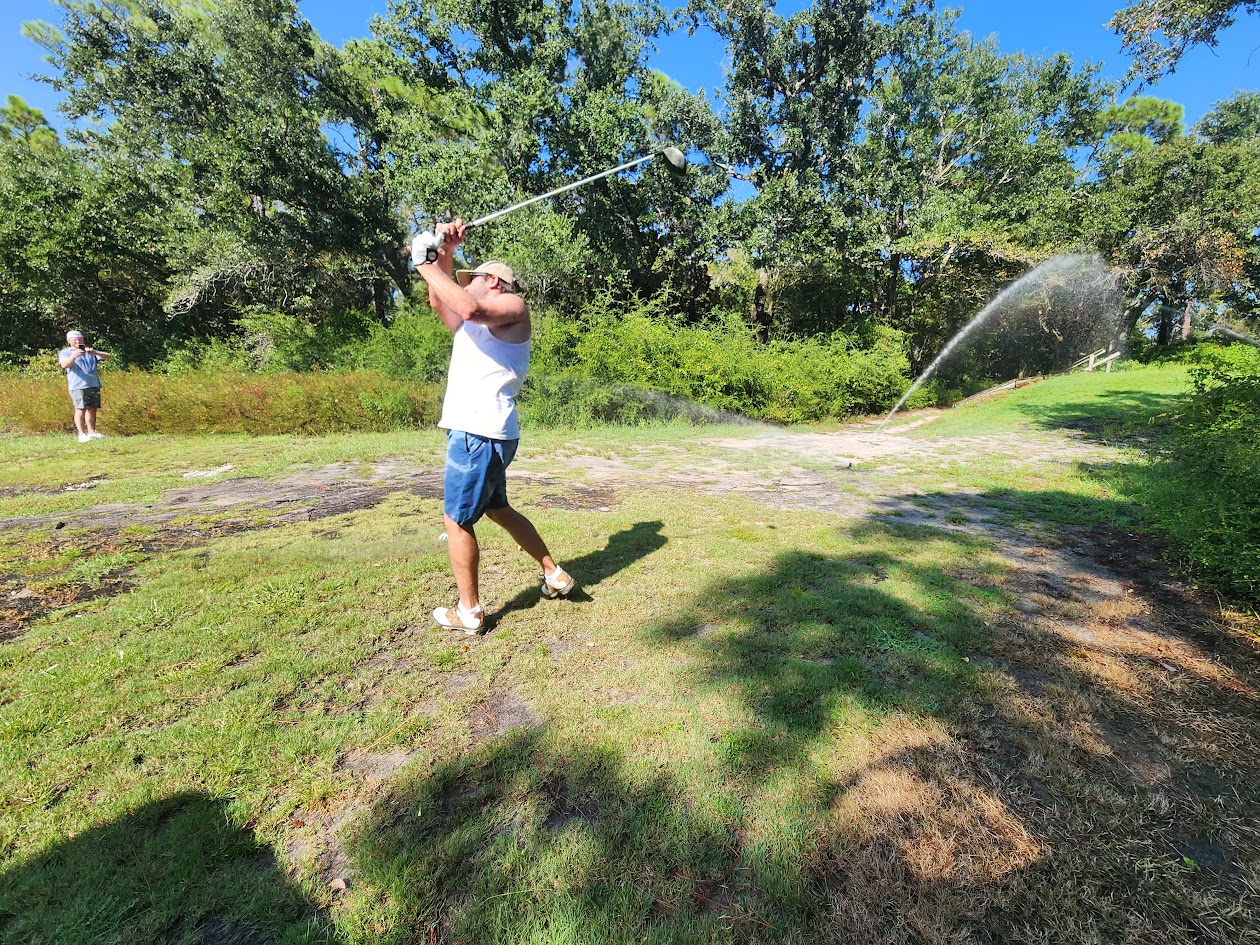 An HFFL owner finishing a golf swing beside a running sprinkler
